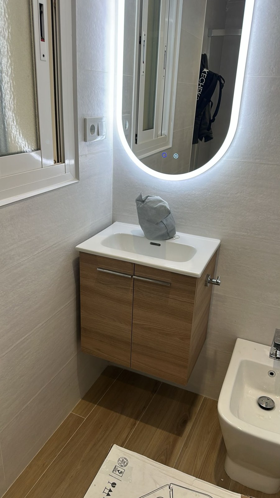 Lavabo con mueble de madera y espejo LED en un baño reformado