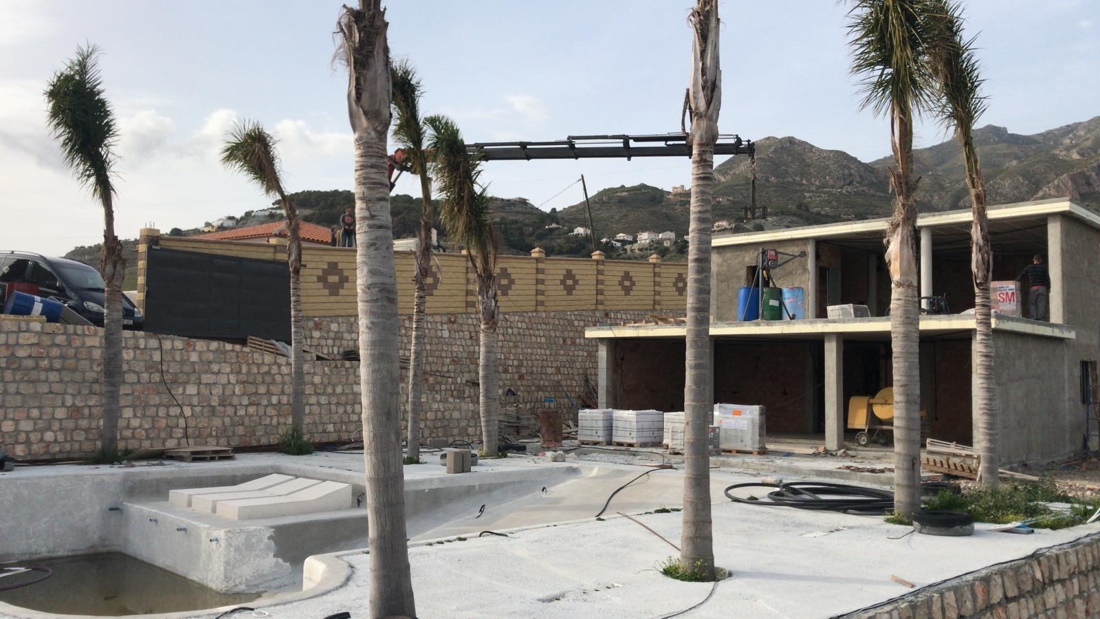 Casa en obra con la piscina en construcción y palmeras