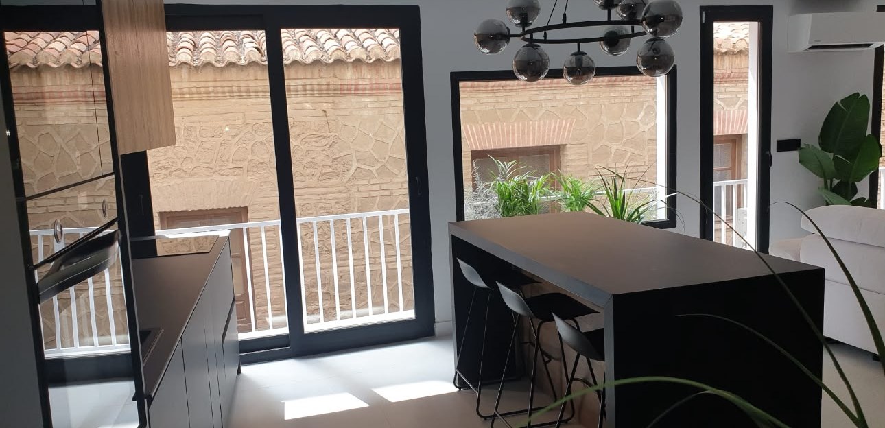 Cocina abierta con isla negra y taburetes junto a los ventanales