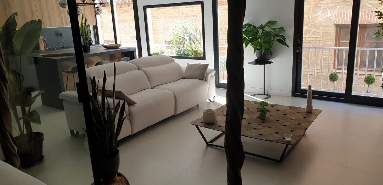 Salón con sofá blanco, ventanales negros y suelo continuo claro