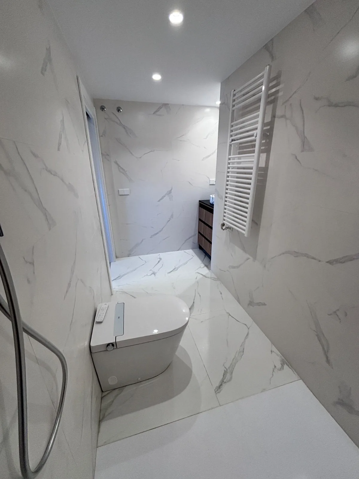 Baño reformado con porcelánico blanco efecto mármol, inodoro suspendido y radiador toallero