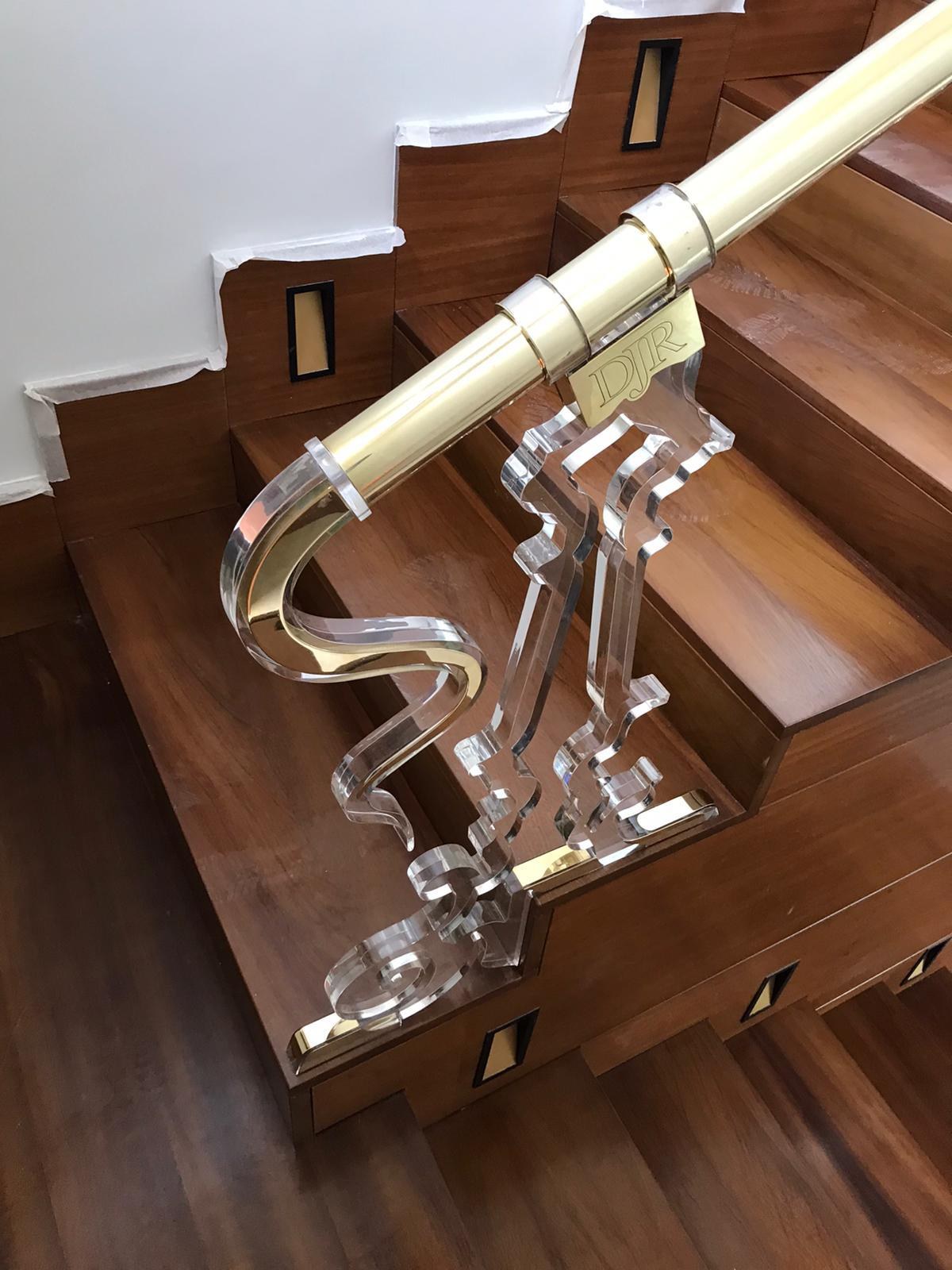 Detalle de escalera de madera con barandilla de vidrio y pasamanos dorado