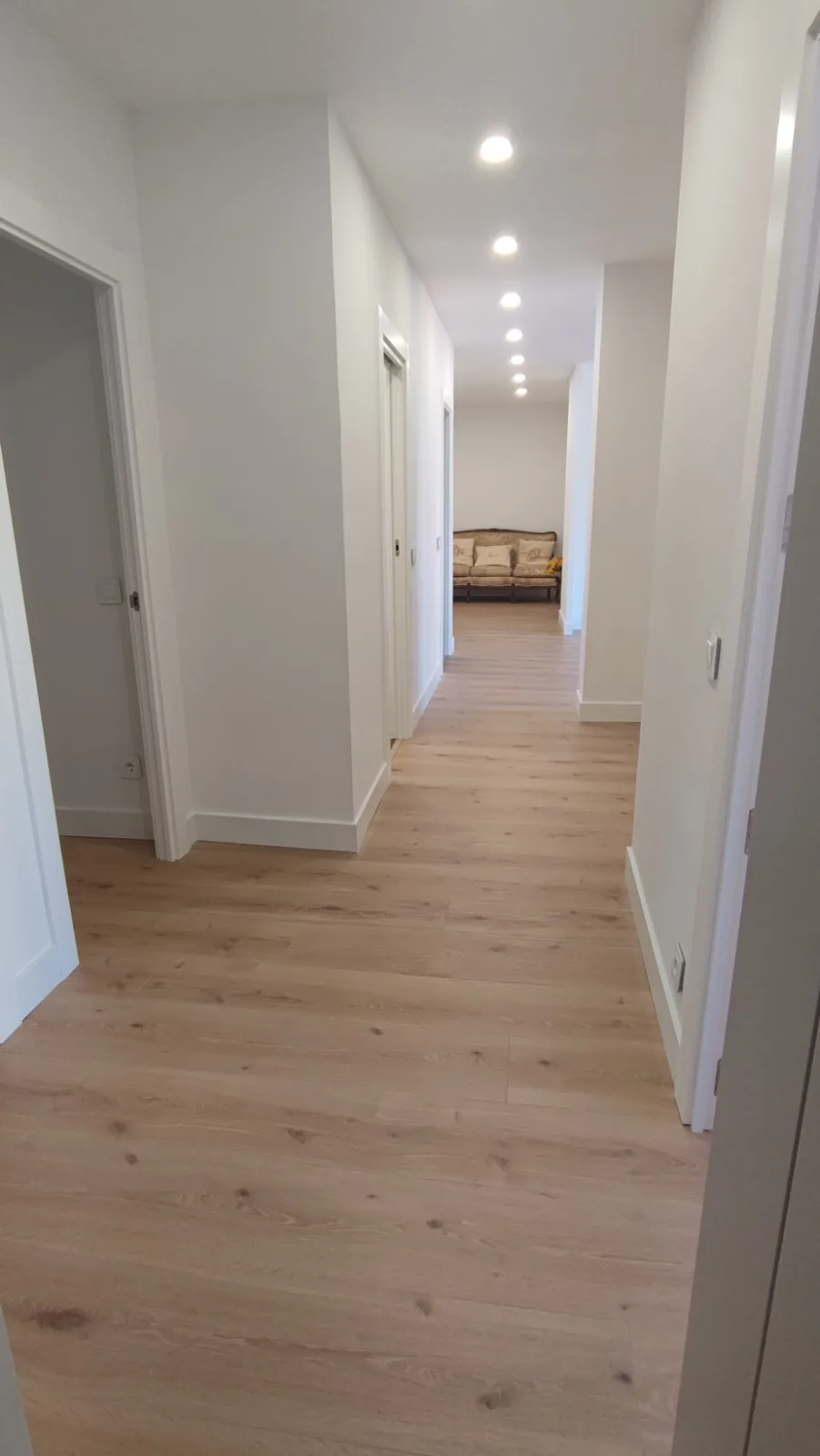 Pasillo largo de vivienda reformada con tarima clara e iluminación empotrada