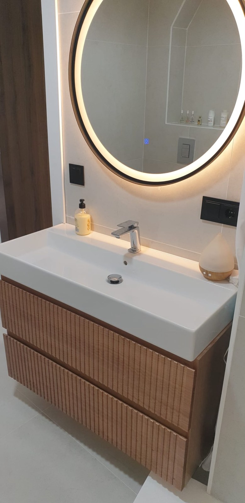 Baño con mueble de madera acanalada y espejo redondo retroiluminado