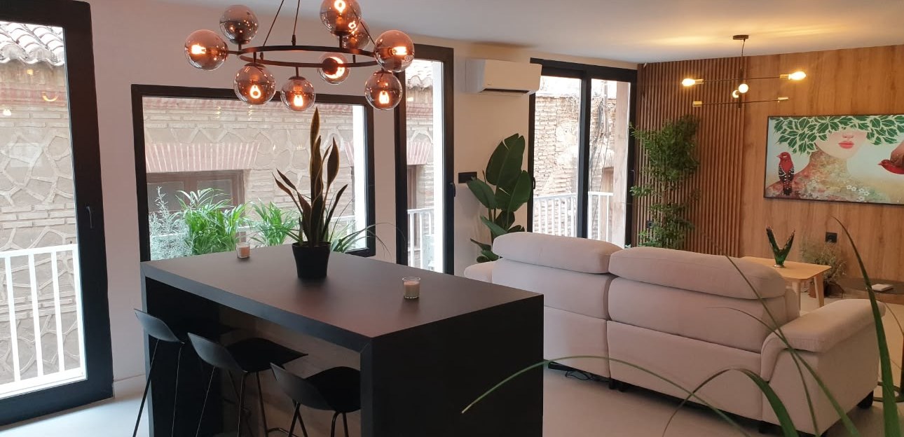 Salón abierto con isla de cocina negra, sofá blanco y pared de listones de madera