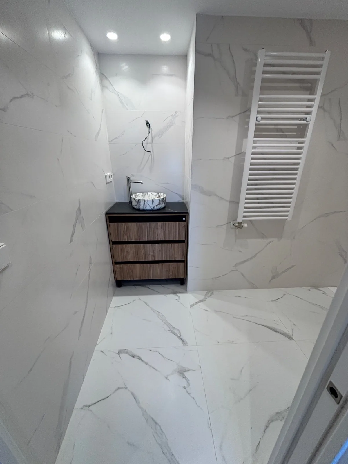 Baño con mueble de madera, lavabo sobre encimera y suelo de porcelánico efecto mármol